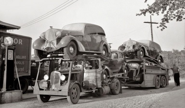 Classic black-and-white image of vintage cars being transported on a truck, showcasing the car shipping process from the past