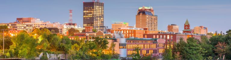A cityscape view of Manchester, New Hampshire, featuring illuminated brick buildings and a tall office tower
