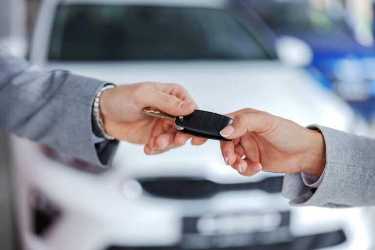 Hands exchanging car keys in front of a white car