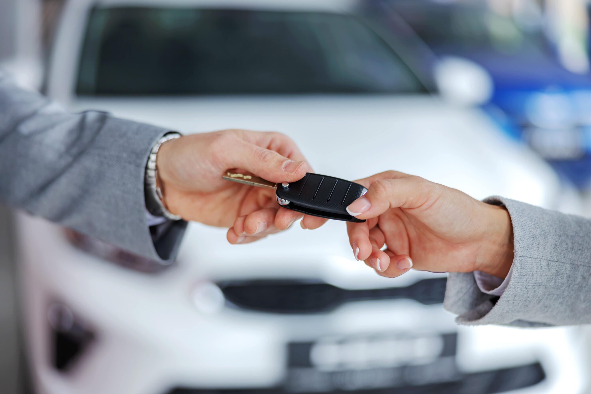 Hands exchanging car keys in front of a white car