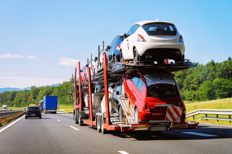 A car carrier truck transporting multiple vehicles on a highway under a clear blue sky.