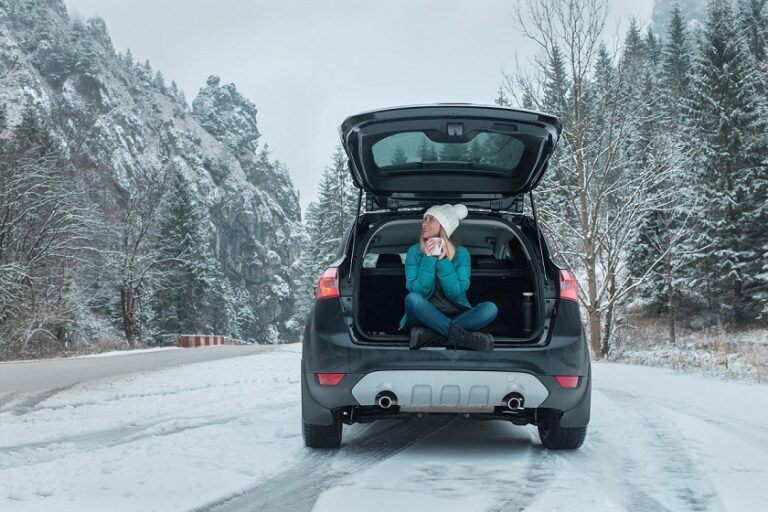 Young woman, a snowbird, sitting in a black car on a snowy winter day, enjoying the view.